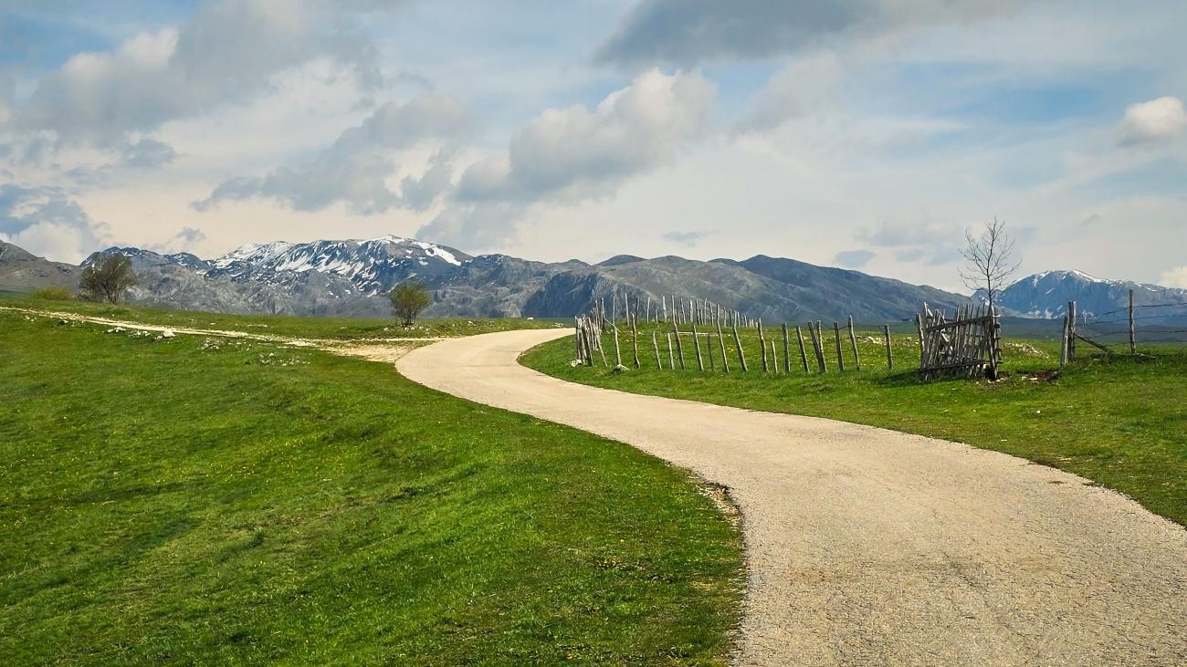 A winding country road leading toward snow-capped mountains in the Montenegrin highlands.