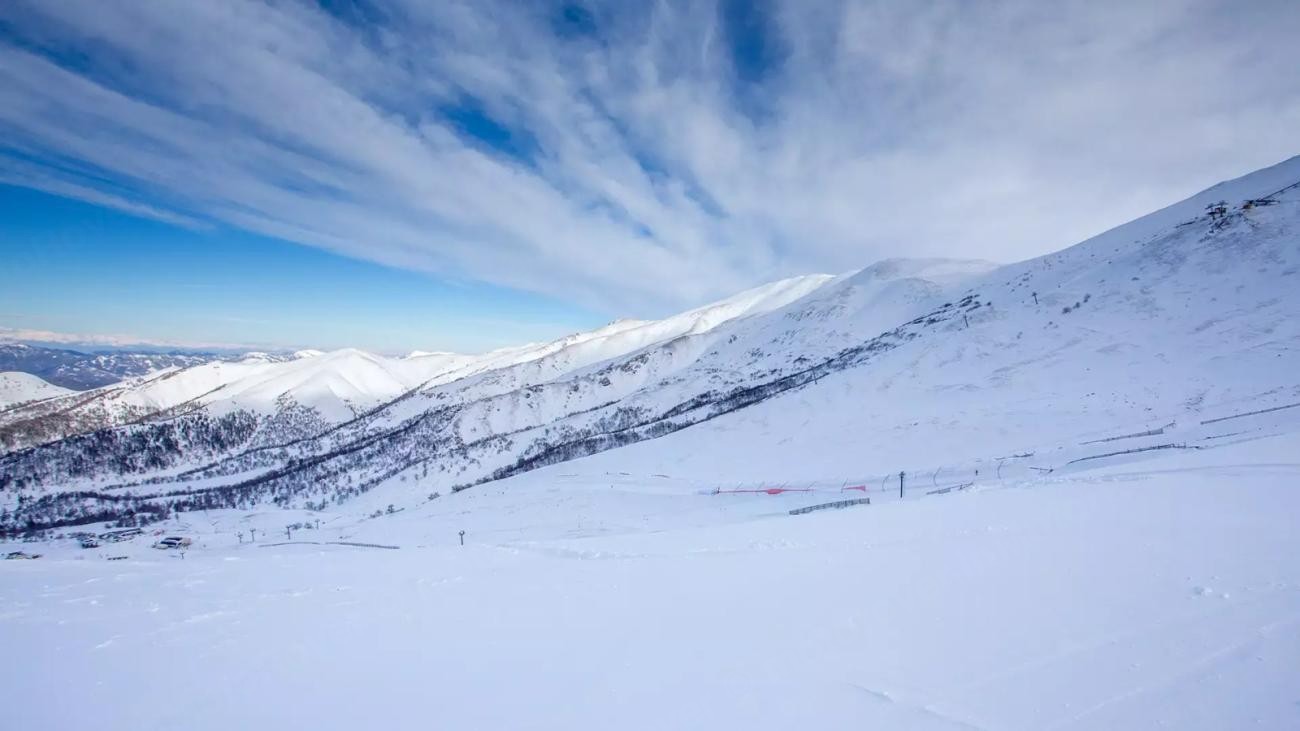 A vast snow-covered ski resort landscape in the Georgian Caucasus under a bright blue sky with wispy clouds