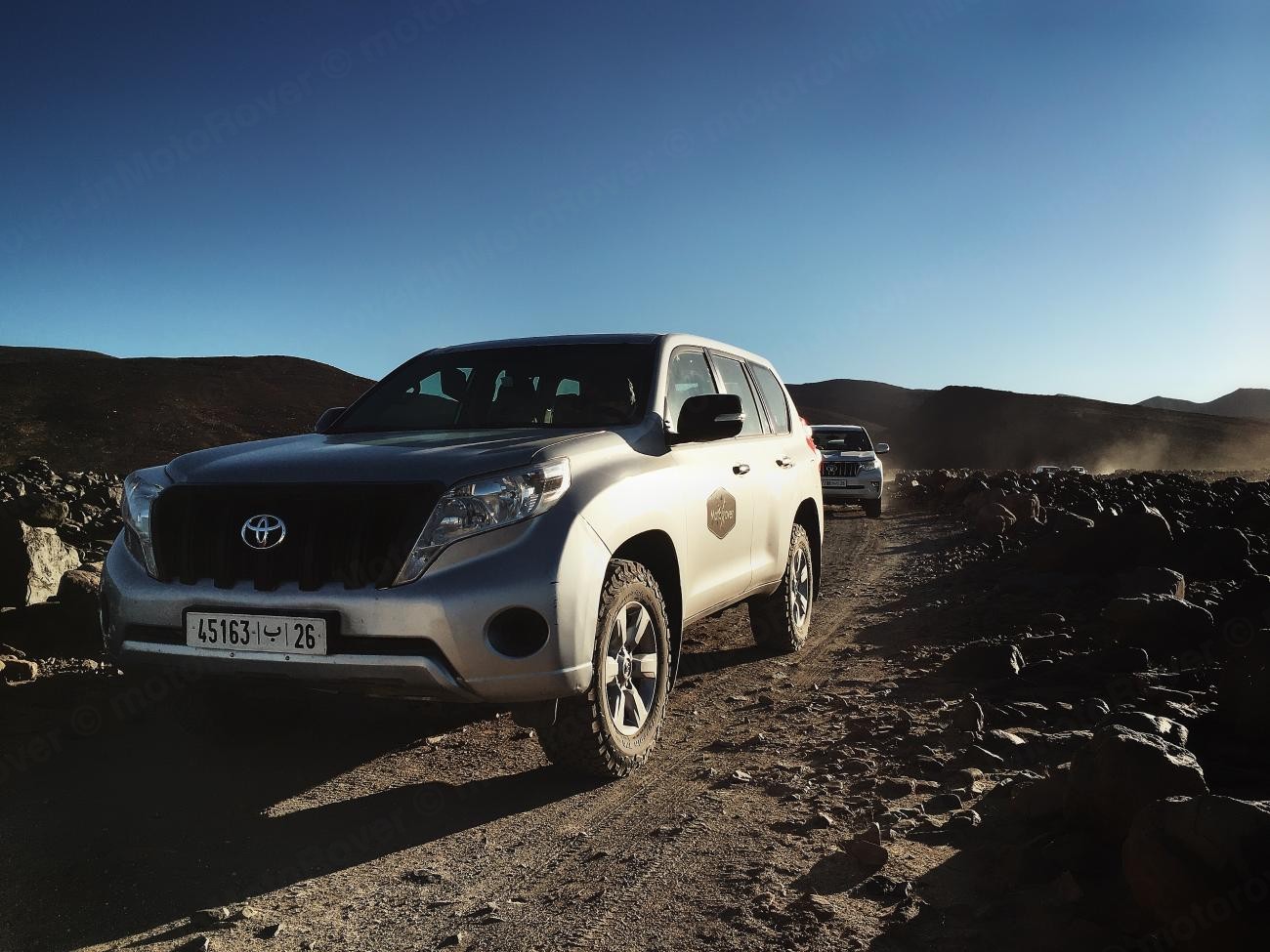 Toyota Land Cruiser navigating a rocky off-road mountain trail in the Moroccan highlands.
