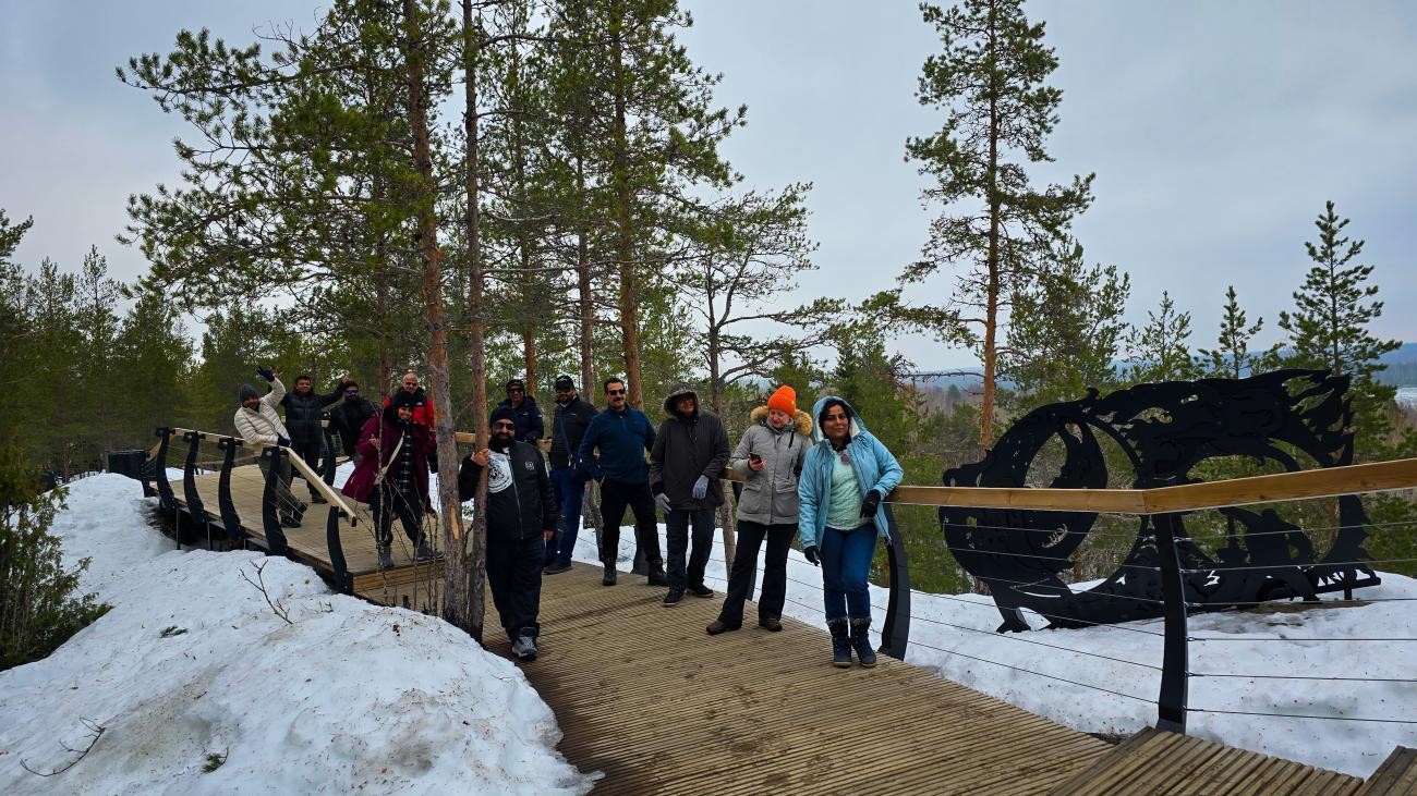A group of tour participants walking along a snowy boardwalk through a pine forest in the Russian Arctic.