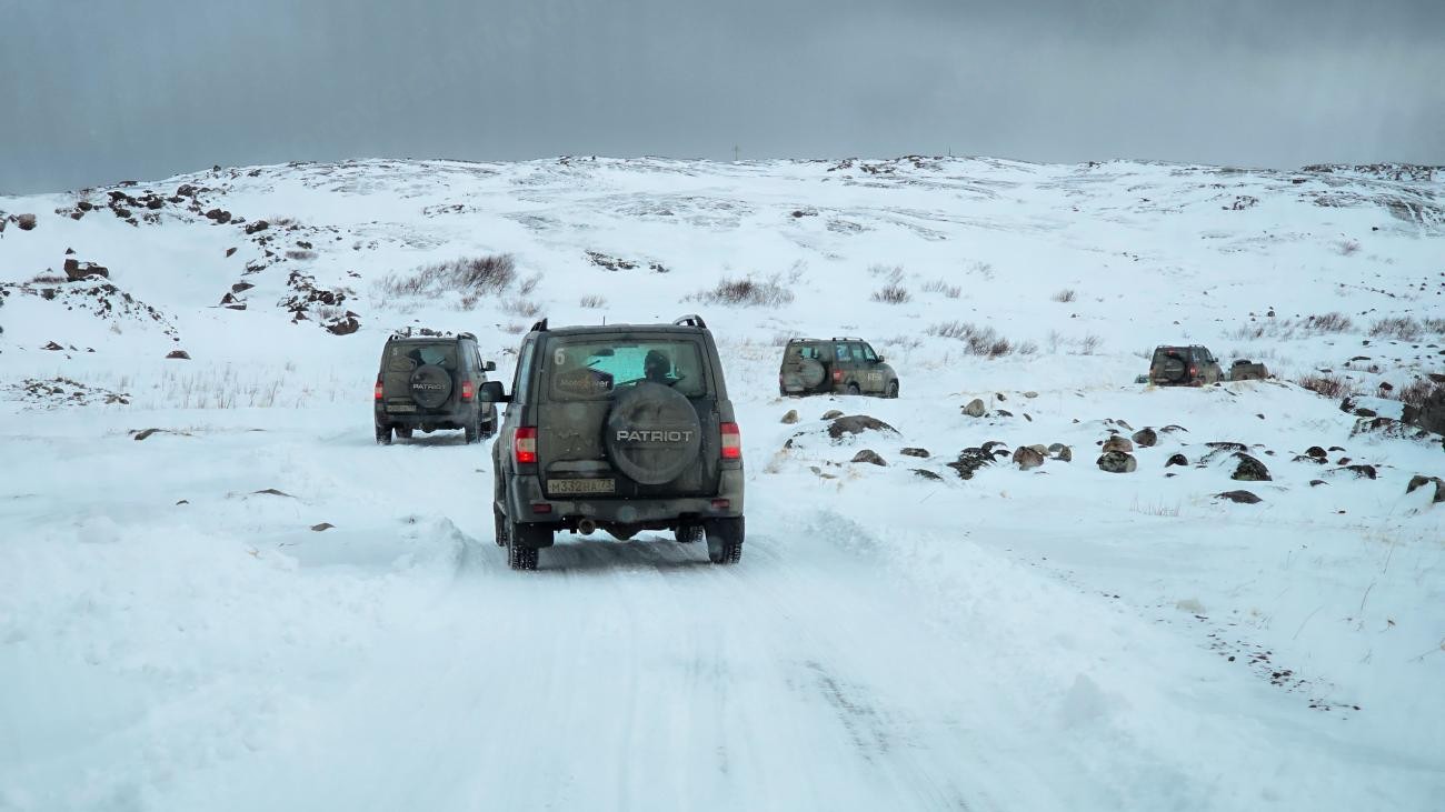 UAZ Patriot SUVs driving in convoy along a snowy off-road trail through the barren Arctic hills.