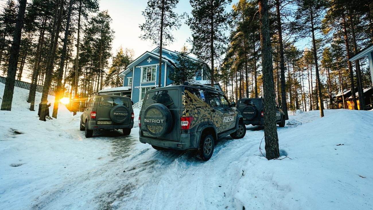 MotoRover SUVs parked outside a blue wooden cabin in a snowy pine forest with golden sunlight filtering through the trees.
