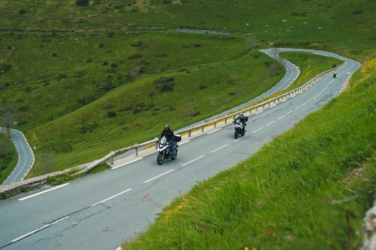 Motorcyclists riding through lush green switchback roads on a French Pyrenees mountain pass.